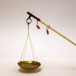 Brass weighing scale with a shallow dish suspended by yellow strings from a long wooden pole with red tassels.
