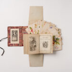 An open book with red patterned inside cover, open pages showing illustrations aside the text 'Cousin Johnny and his india nurse' and scattered floral cards on a cream background.