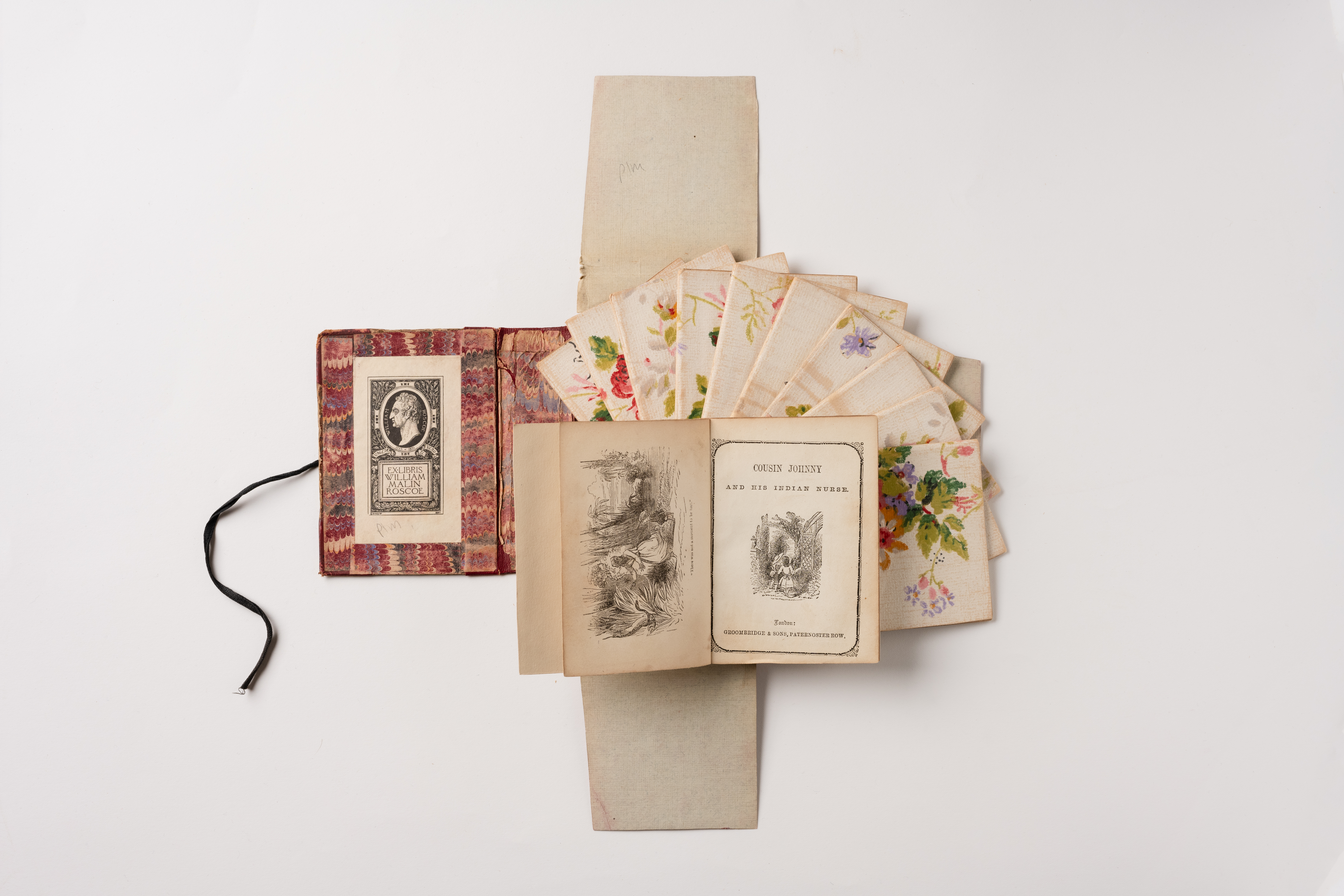 An open book with red patterned inside cover, open pages showing illustrations aside the text 'Cousin Johnny and his india nurse' and scattered floral cards on a cream background.