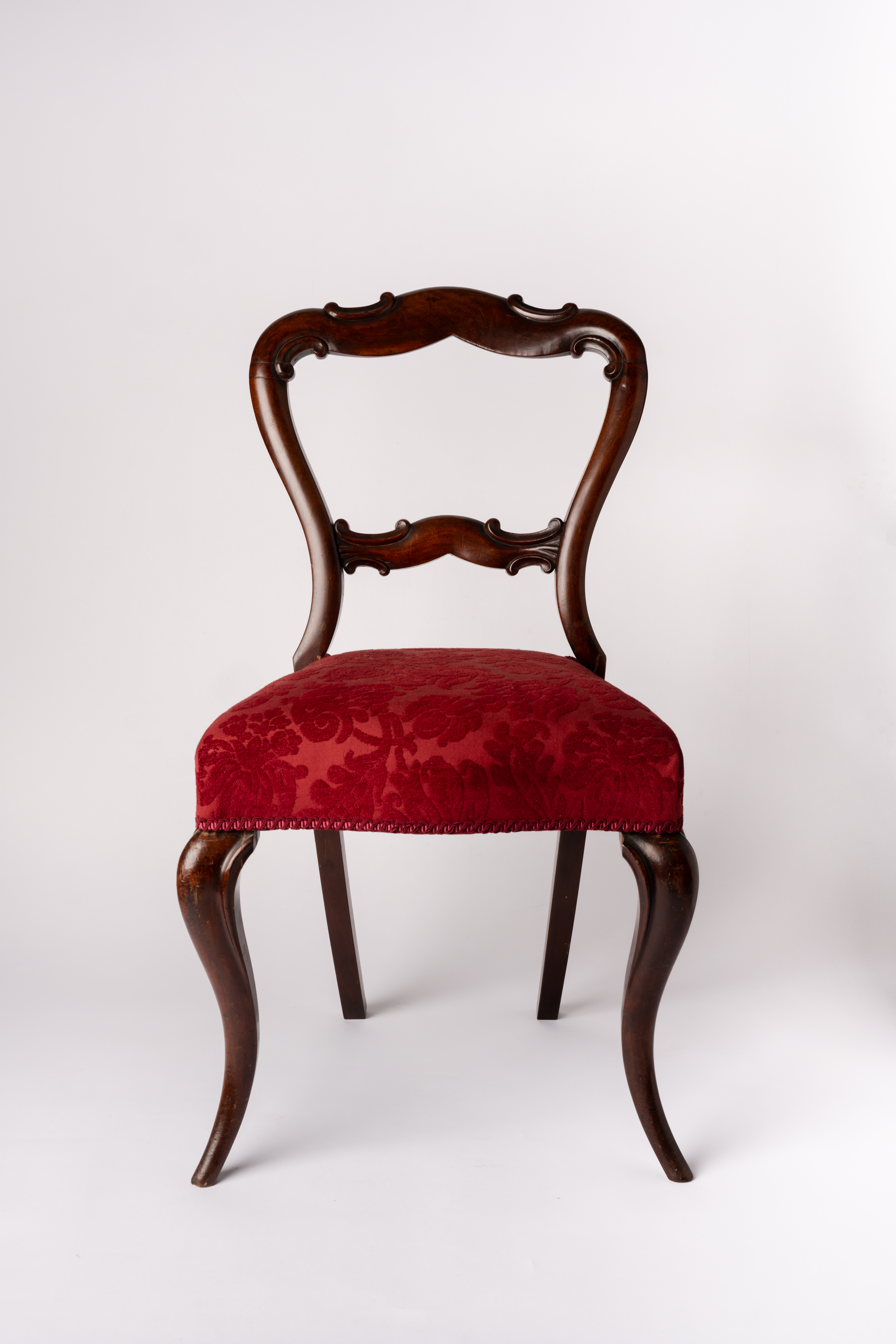 A mahogany chair with an open, rounded splat back; its front legs form S-shaped curves, and it is topped with a plush, red patterned upholstered seat, shown against a plain white background.
