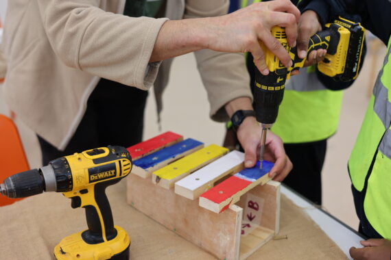 Adult and children hands drilling a wooden homemade xylophone in a workshop