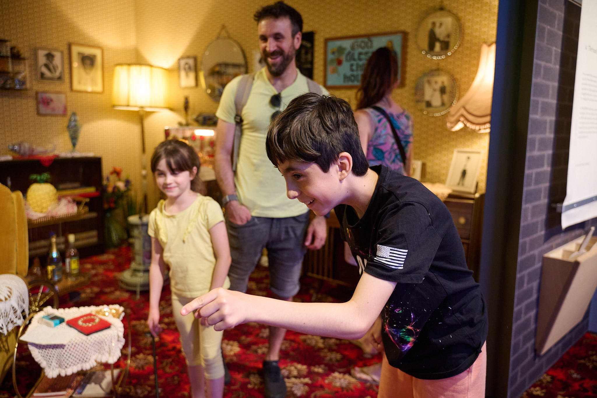 A family in A Terraced House in 1978 installation at the Museum; a smiling child leans forward to point at something outside the frame while the other child and one of the adults watch with smile.