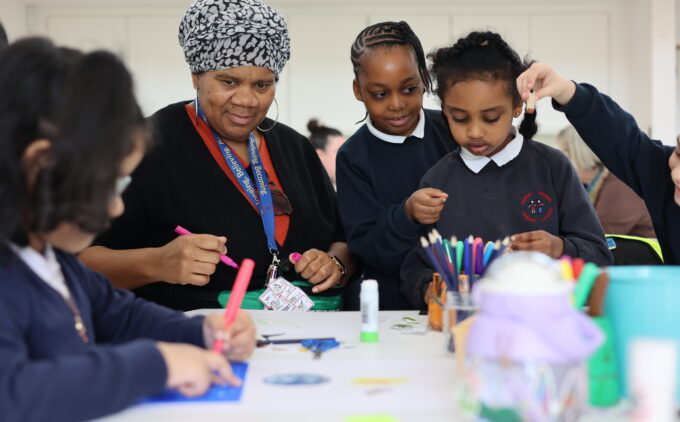 An adult guides primary school children in a creative workshop, as they draw with markers and coloured pencils around a table at the Museum.