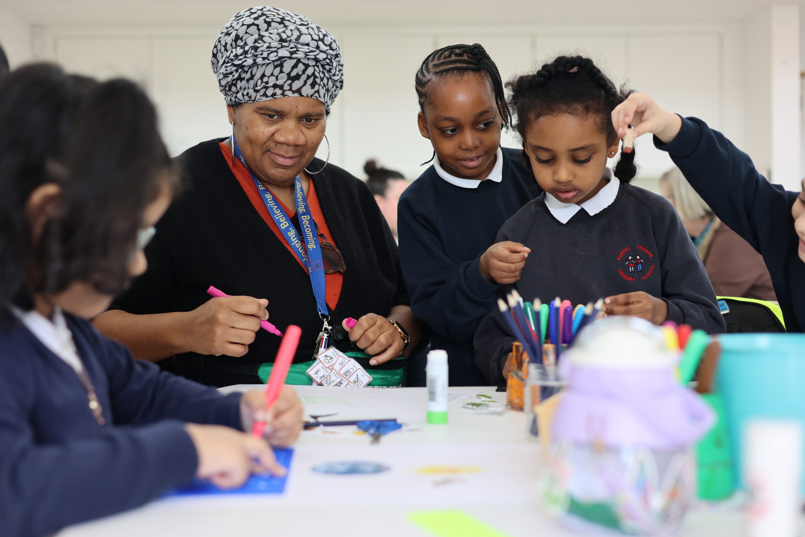 An adult guides primary school children in a creative workshop, as they draw with markers and coloured pencils around a table at the Museum.