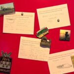Multiple white recipe cards with handwritten recipes pinned to a red panel by souvenir magnets - a Fry’s Chocolate fairy, a camel and pyramids, Stirling Castle, a steam train, and a sunset sailboat - each answering “What is your favourite meal to cook or eat at home?”