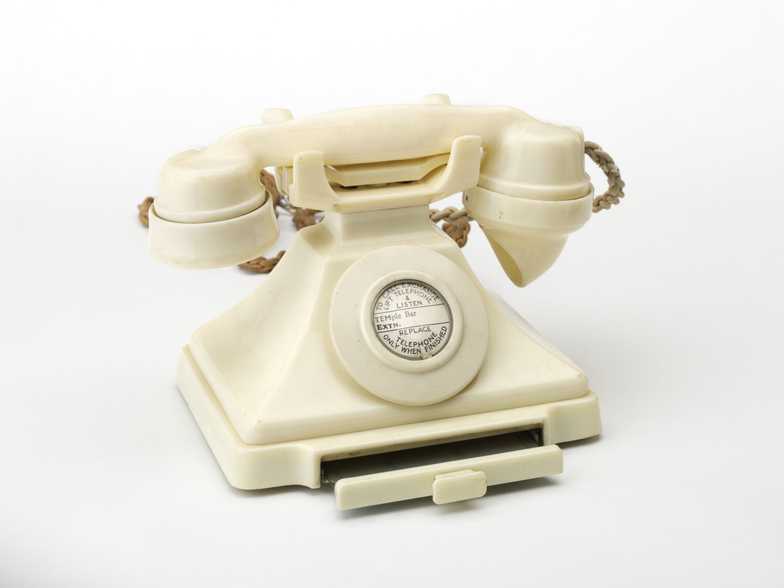 A cream-colored rotary telephone with a rounded handset, circular dial in the centre and a small drawer at the bottom.