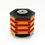 Rotating cassette holder on a white background: black hexagonal top and base sandwich five stacked bright-orange sliding trays, with “cass-bar” written in black on a white circular label centered on the top.