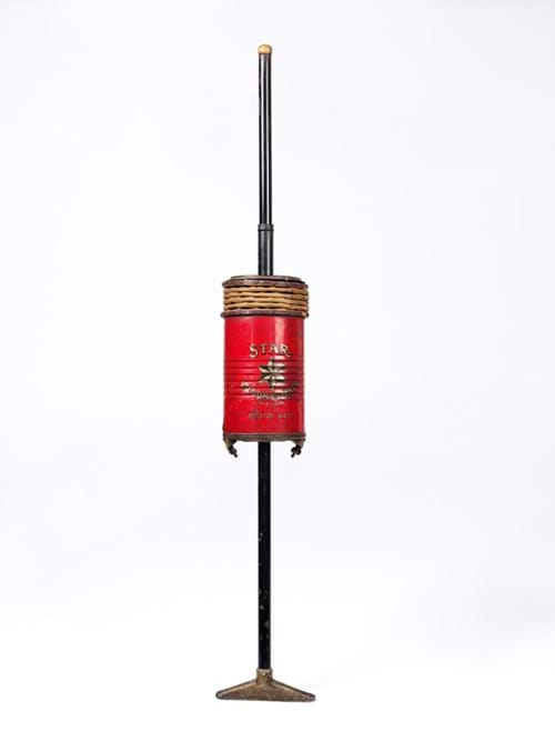 Red cylindrical vacuum cleaner with long black handle and brass fittings