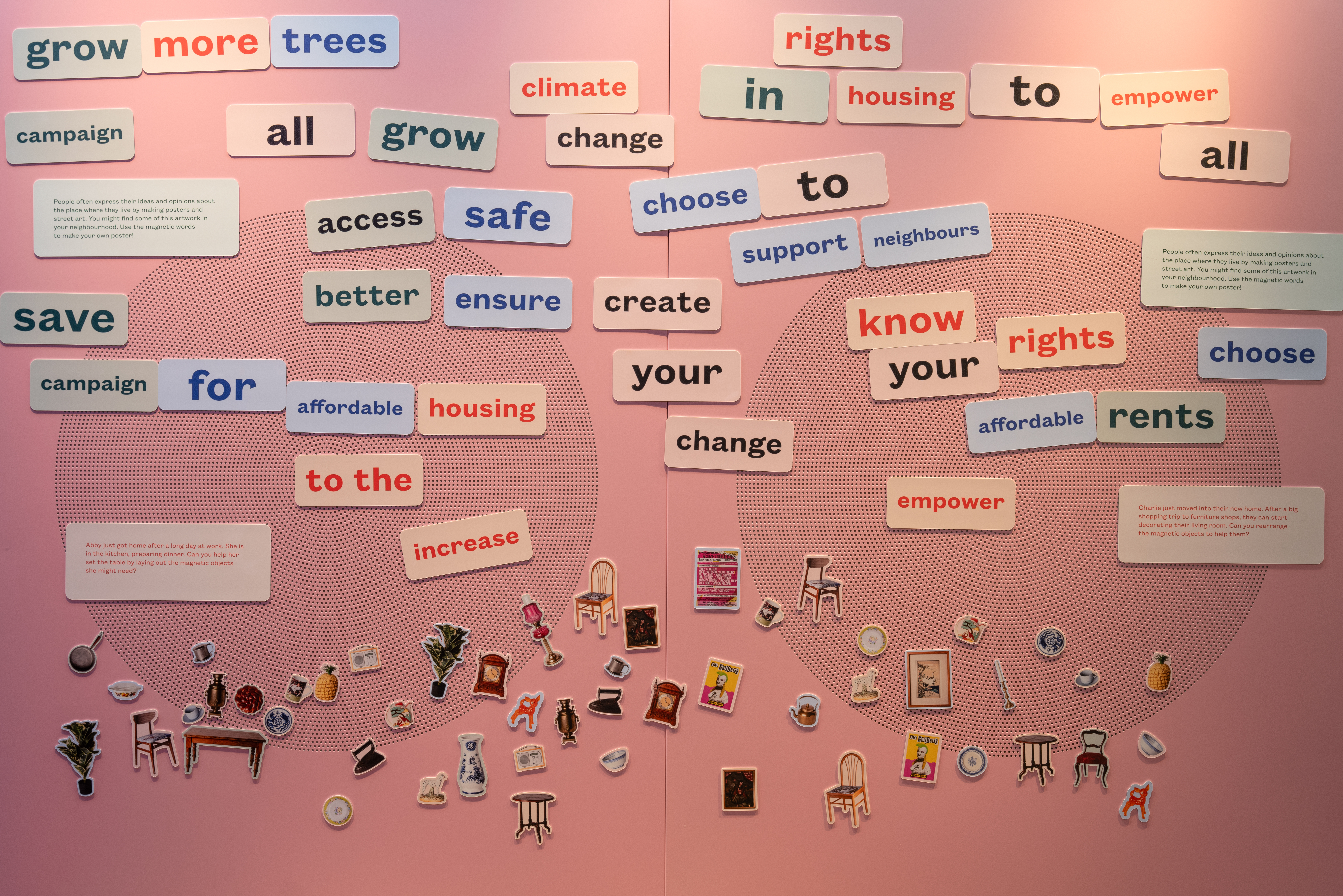 An interactive pink wall installation covered in individual word magnets placed side by side to form phrases like “grow more trees,” “rights in housing,” and “know your rights,” with household object cut out magnets, such as chairs, vases, and more, scattered along the bottom.