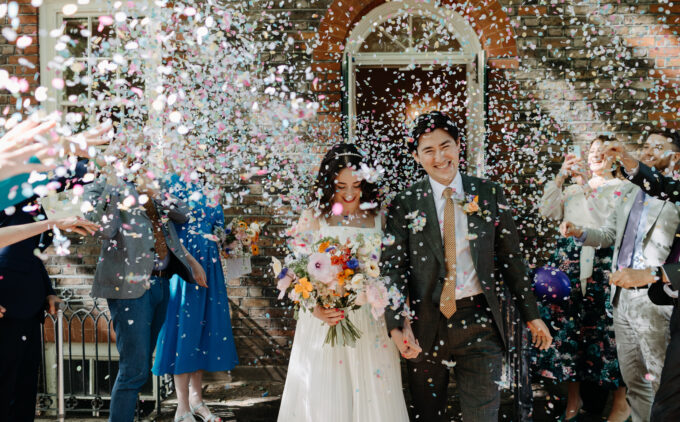 A couple walk together and smile after getting married, with their friends and family throwing white confetti