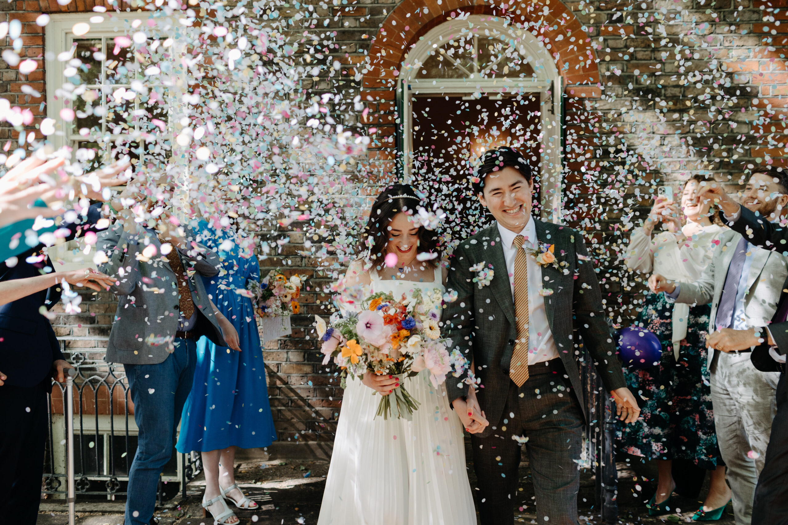 A couple walk together and smile after getting married, with their friends and family throwing white confetti