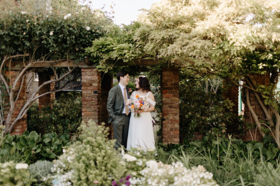 A couple standing in the middle of a brick arch in a lush garden
