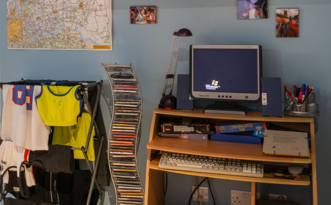 A 2000s computer sits on a desk. A CD stand, drying laundy and a map are visable.