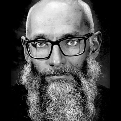 Black and white photo of a man with a beard and glasses staring at the camera.