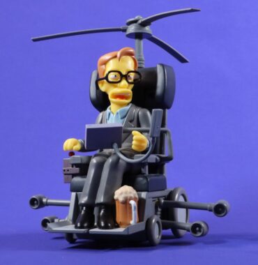 A cartoon-style action figure of Stephen Hawking in a futuristic wheelchair with helicopter rotor blades and a pint of foamy beer by his left foot. The look is based on his appearance in The Simpsons. Set against a plain purple background.