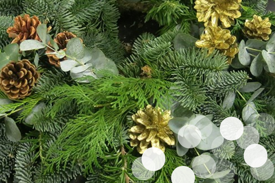 A close-up of a festive wreath made from fresh evergreen sprigs and cedar boughs, interspersed with eucalyptus leaves and pine cones—some left natural, others painted gold—for a seasonal, textured arrangement.