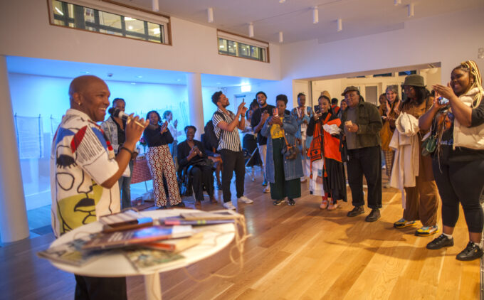A man speaking into a microphone to a crowd of attendees listening in a modern white-walled space.