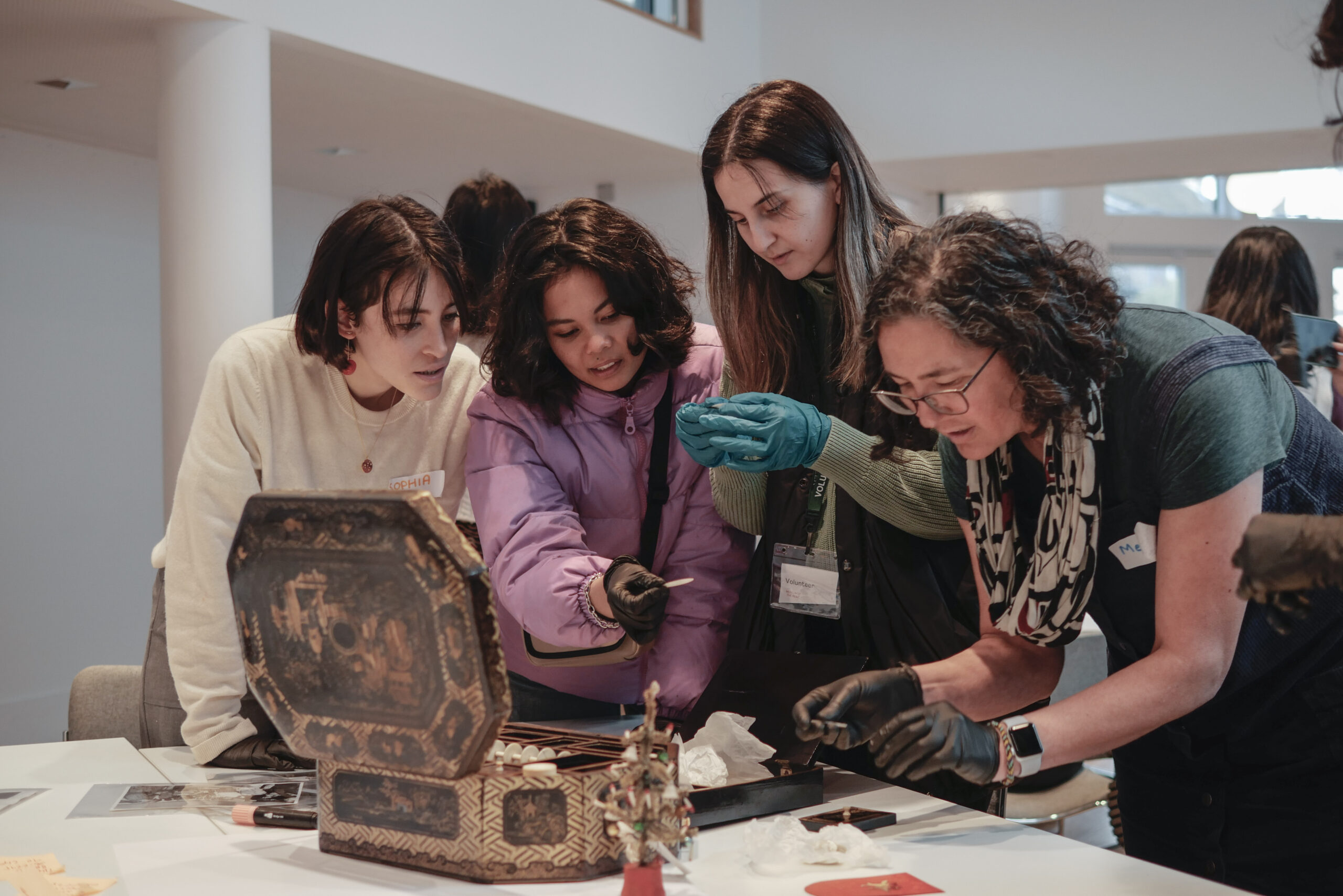 People gathered around an enameled chest, holding items with gloves