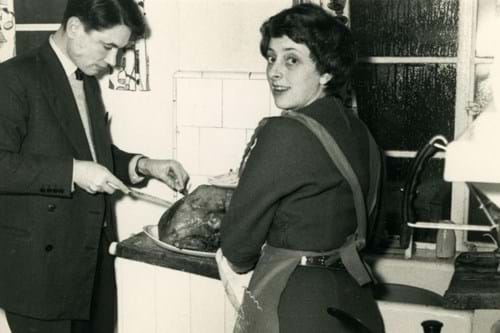 Black and white photo of man carving turkey while woman helps in kitchen