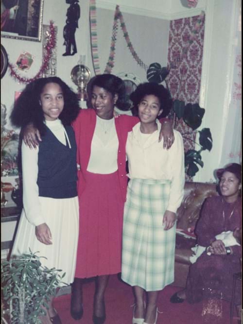 Three young women posing together in 1970s-style clothing and hairstyles in a decorated room