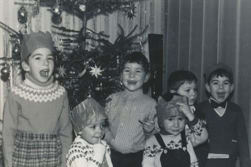 Black and white photo of children in winter sweaters posing by Christmas tree