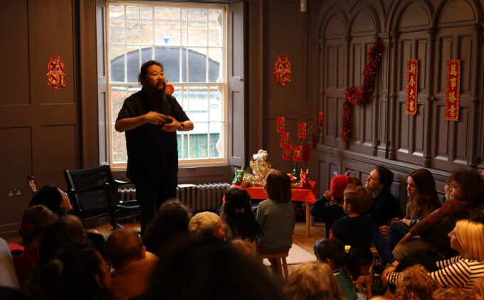 Children sit on stools watching a man motion to them.
