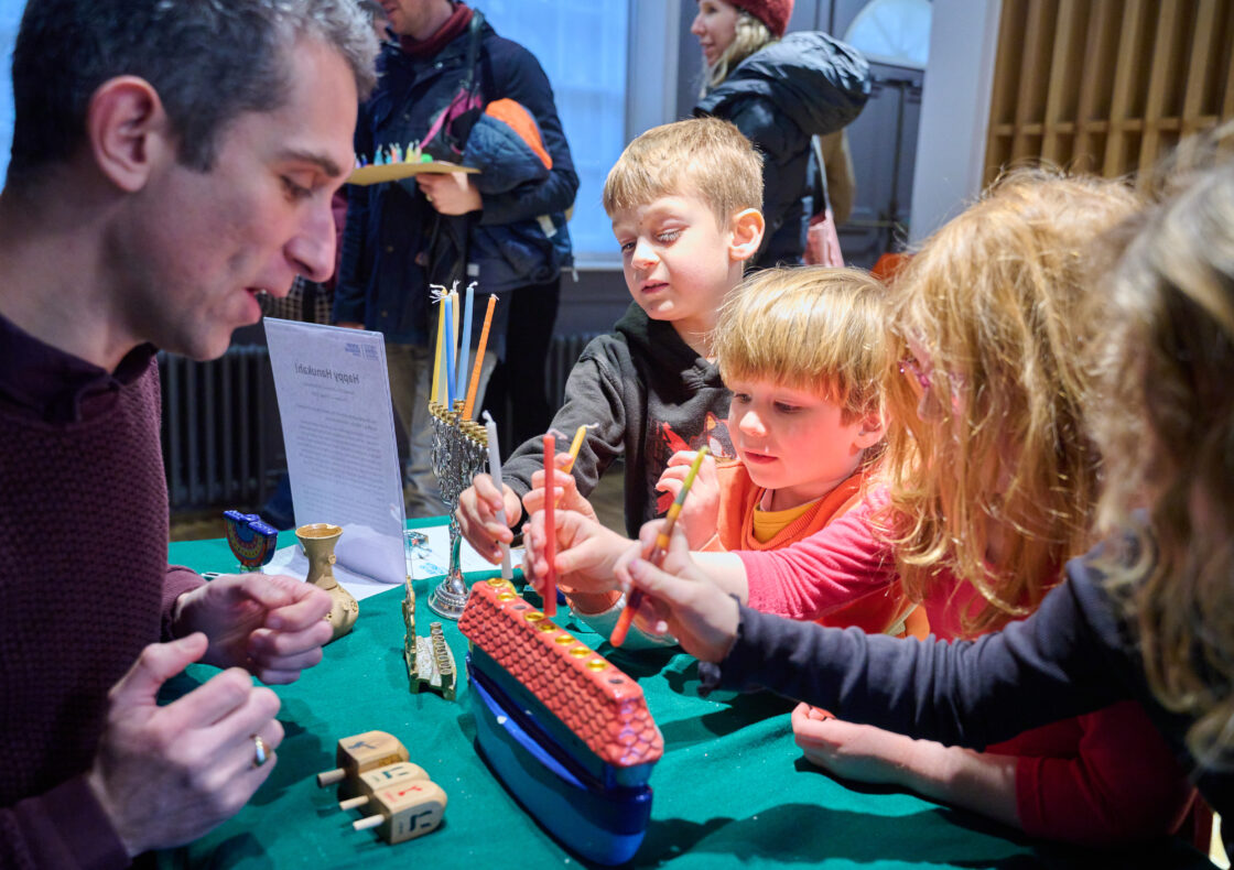 An adult speaks to interested children about a multicoloured menorah