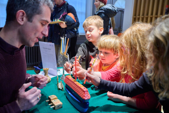 An adult speaks to interested children about a multicoloured menorah