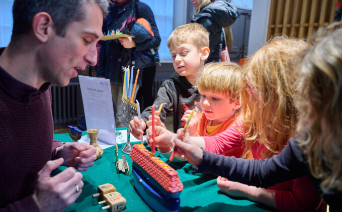 An adult speaks to interested children about a multicoloured menorah