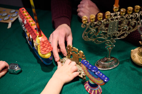 An adult hand and a child's hand reach for an object next to a model of a menorah