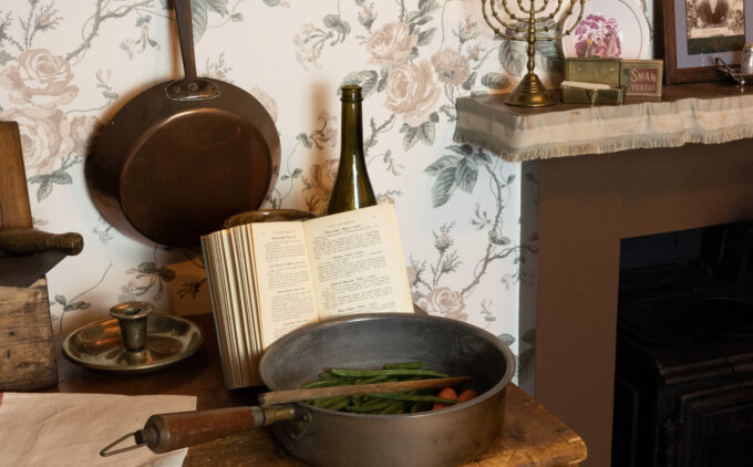 Close up view of a pot with ingredients and a recipe book. There is a menorah on the fireplace mantel.