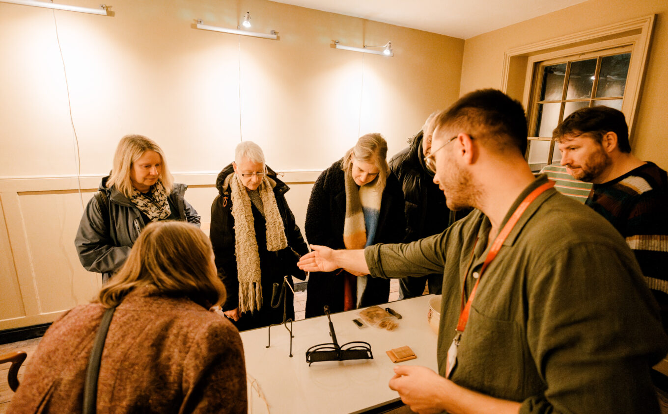 A group of people standing around a table with a curator gesturing at historical objects