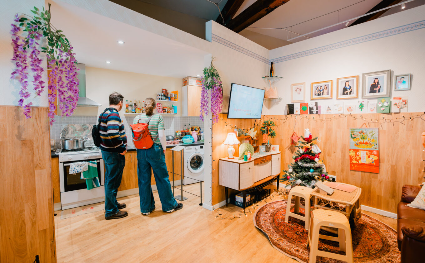 Two people standing in a room set of a living room and kitchen
