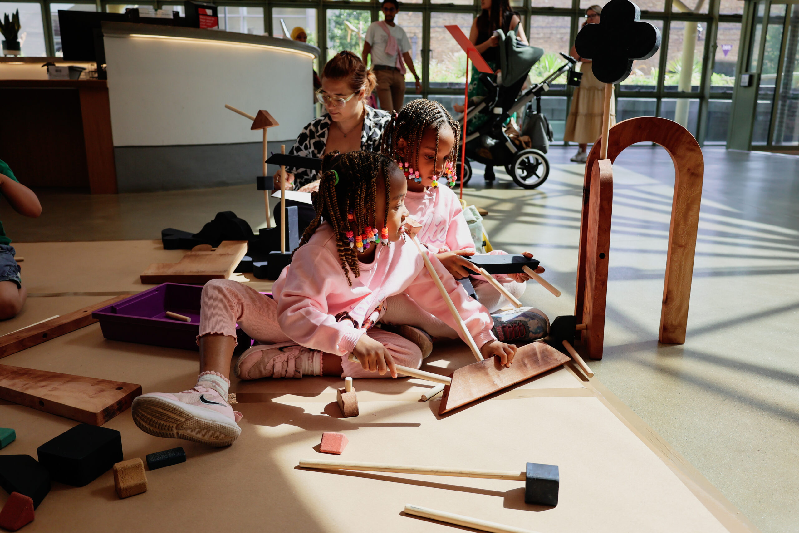 Children sitting on the floor of a museum atrium playing with wooden blocks creating structure
