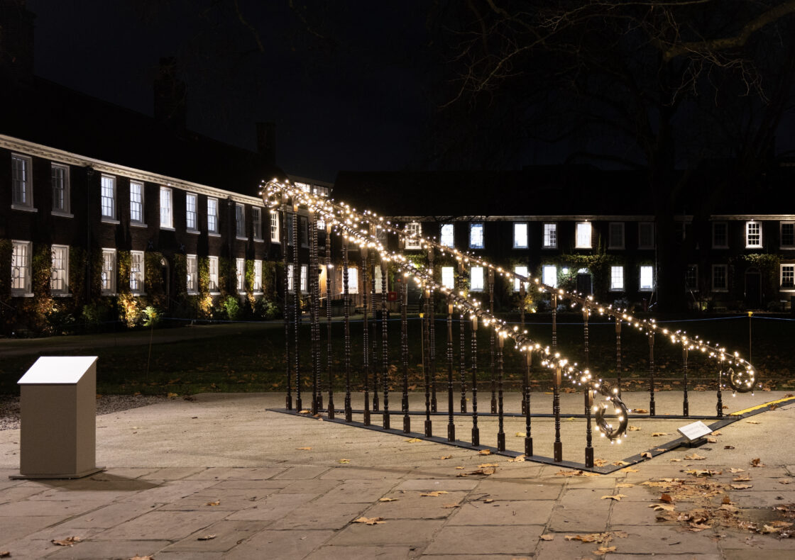 An installation artwork with banisters and fairy lights is placed in front of Almshouse buildings.