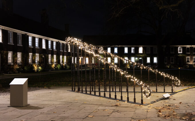 An installation artwork with banisters and fairy lights is placed in front of Almshouse buildings.