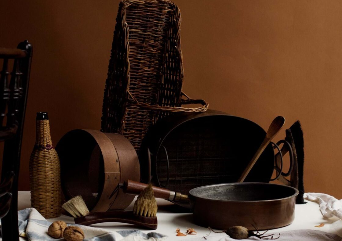 A wooden table topped with tablecloth and kitchen fabrics. On top of the table are different items used in a Tenement Flat in 1913 in a Jewish household including a pan and a frying pan. The overall tone is brown.