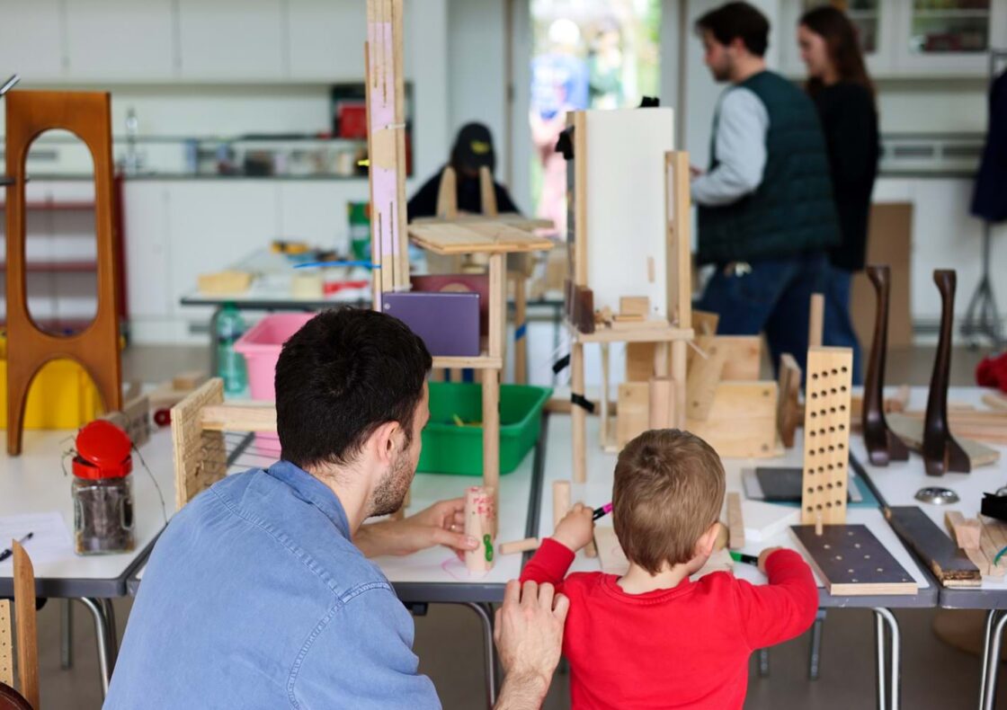 An adult and a child are building an architectural structure with wooden blocks of various shapes.