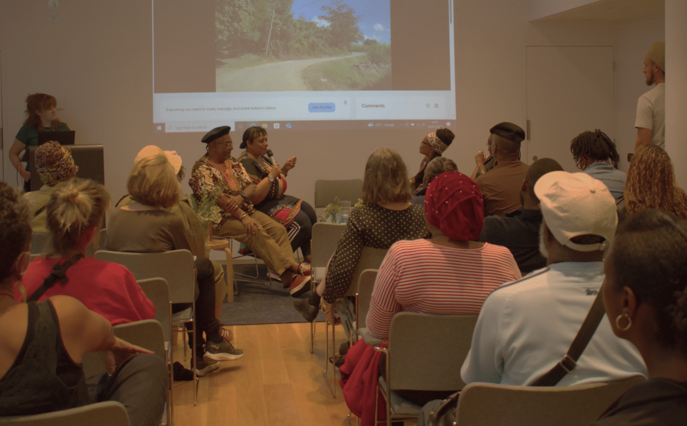 a group of panels sit in front of a projected screen and a group of audience