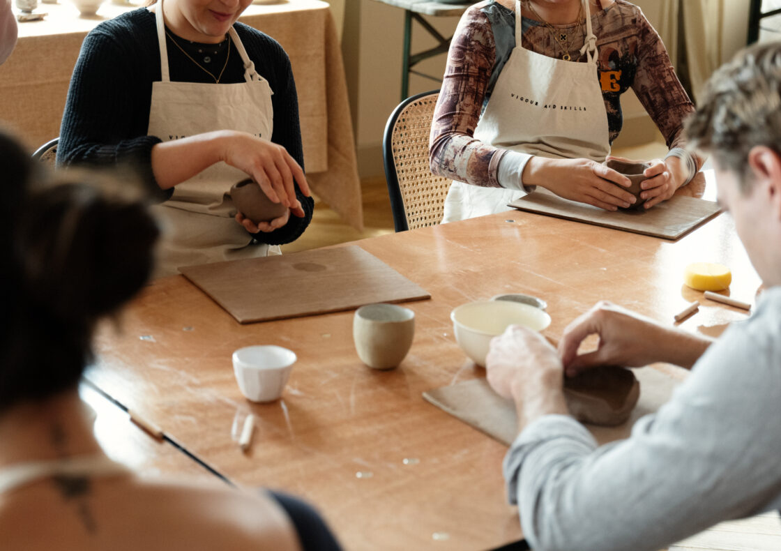 A photograph of a pottery workshop focussed on peoples hands moulding clay pots.