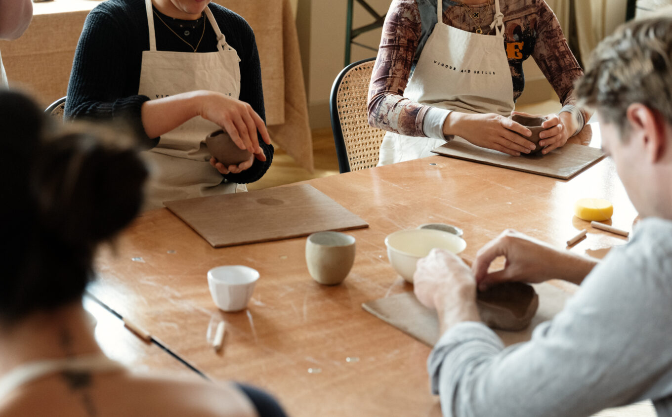 A photograph of a pottery workshop focussed on peoples hands moulding clay pots.
