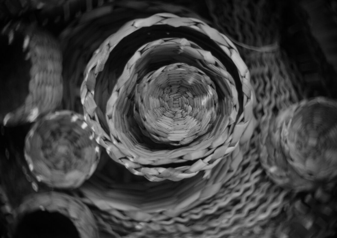 A black and white photography of circular rush baskets, some inside of bigger ones, others next to each other.