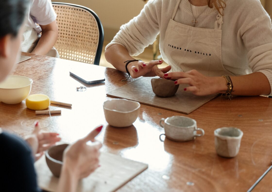 A photograph of a pottery workshop focussed on peoples hands moulding clay pots.