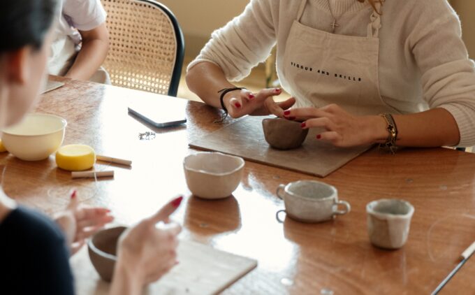 A photograph of a pottery workshop focussed on peoples hands moulding clay pots.