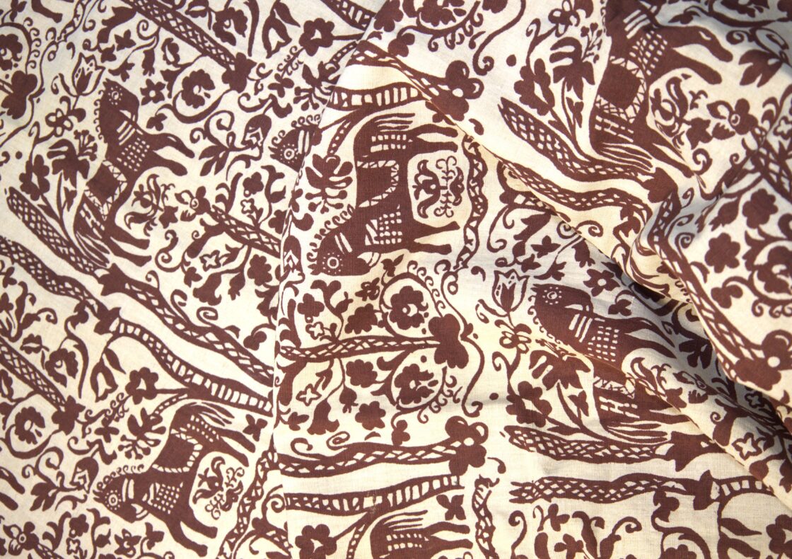 A close up photograph of a curtain with a repeated purple horse print alongside floral and folk motifs