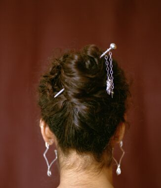 The back of a persons head, with embellished hair pins and silver hanging earings.