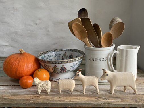 miniature wooden animals displayed on a wood table top beside some kitchen ceramics, pumpkins and wooden kitchen spoons