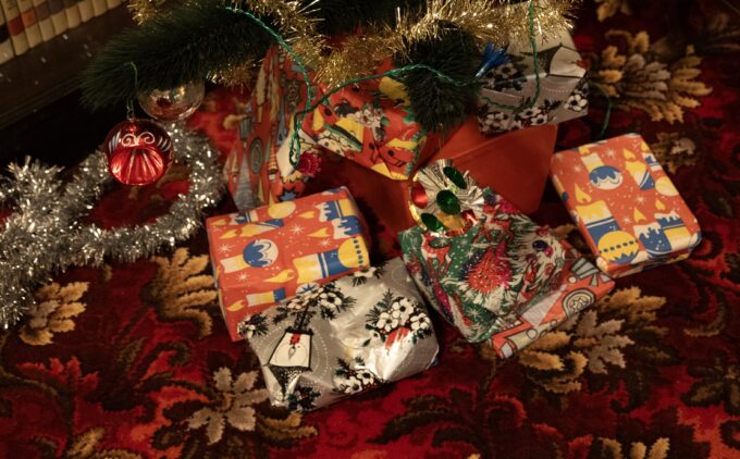 A close up of wrapped presents under a christmas tree, decorated in tinsel and colourful baubles.