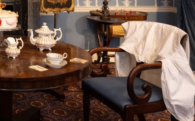 A close up of a table with teapots and cards, and clothes draped over the chair beside it.